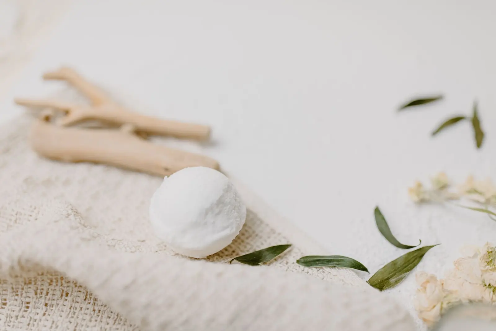 A white bath bomb with driftwood and leafy branches on fabric