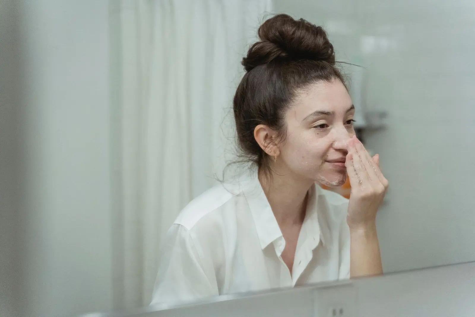 A woman applying facial cream in front of a bathroom mirror