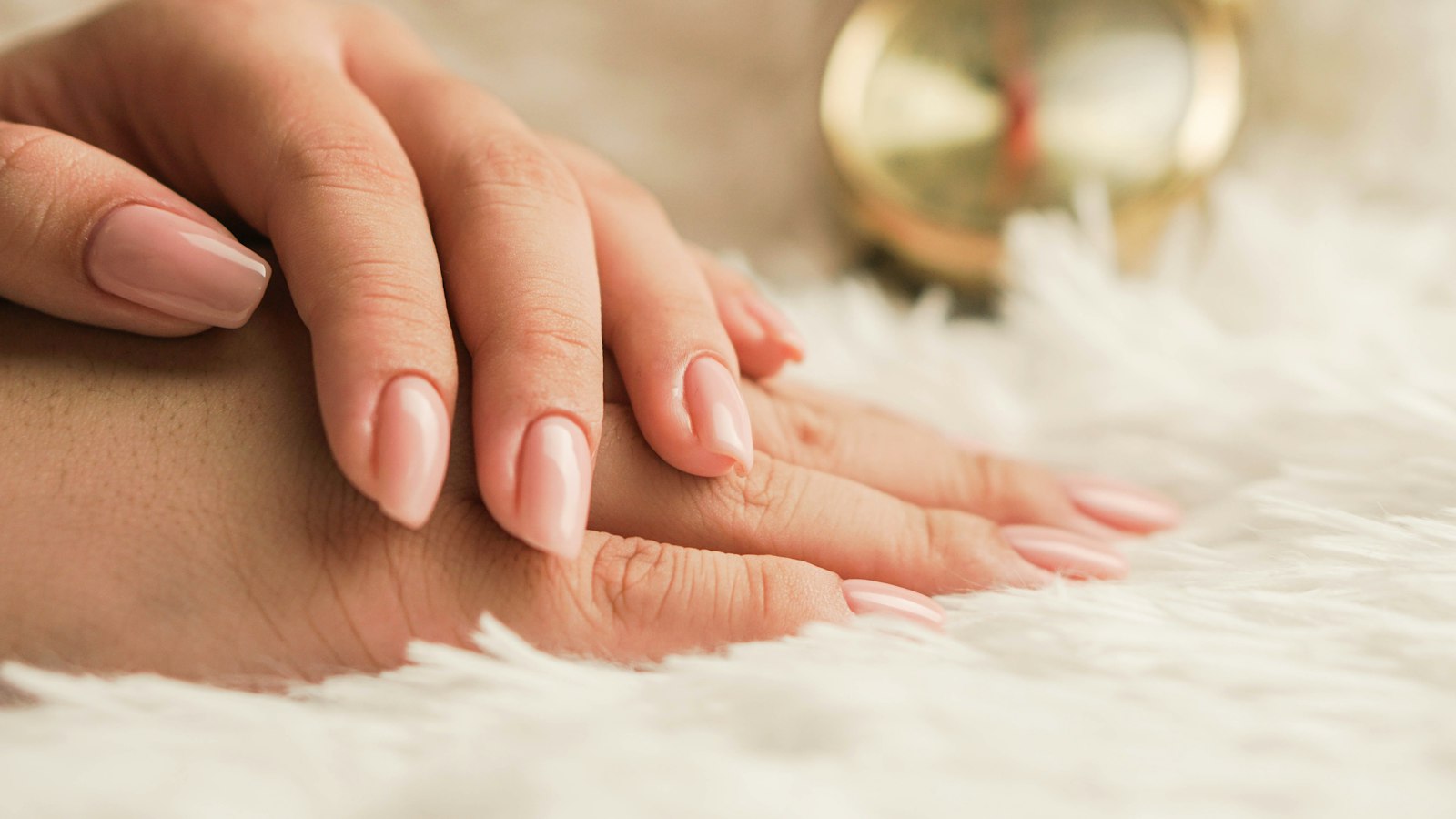 Hands with a soft pink manicure resting on white faux fur