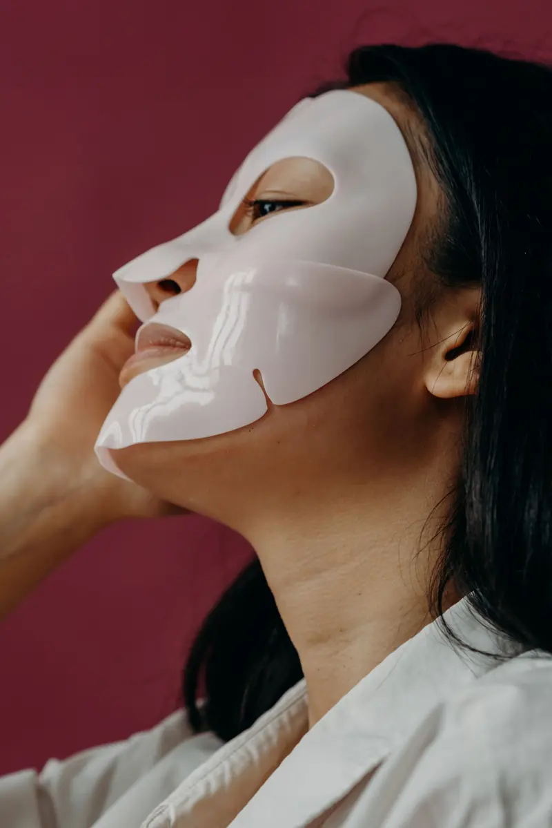 Close-up portrait of an Asian woman enjoying skincare with a sheet mask.
