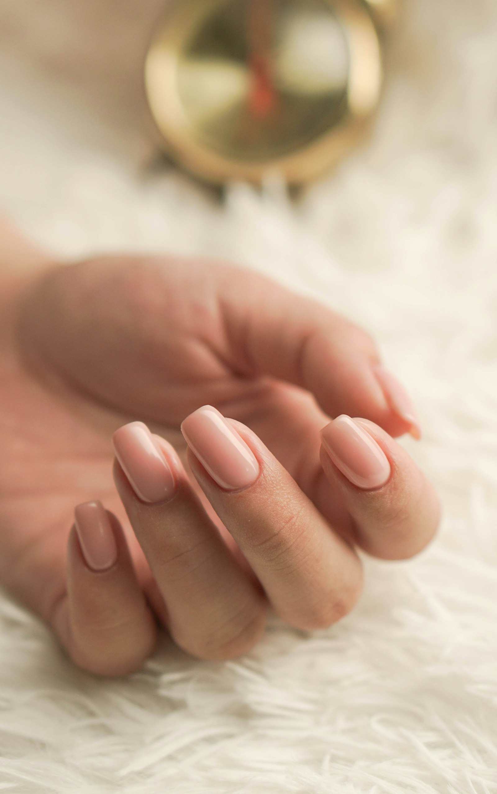 A hand with light pink manicured nails on a soft white surface