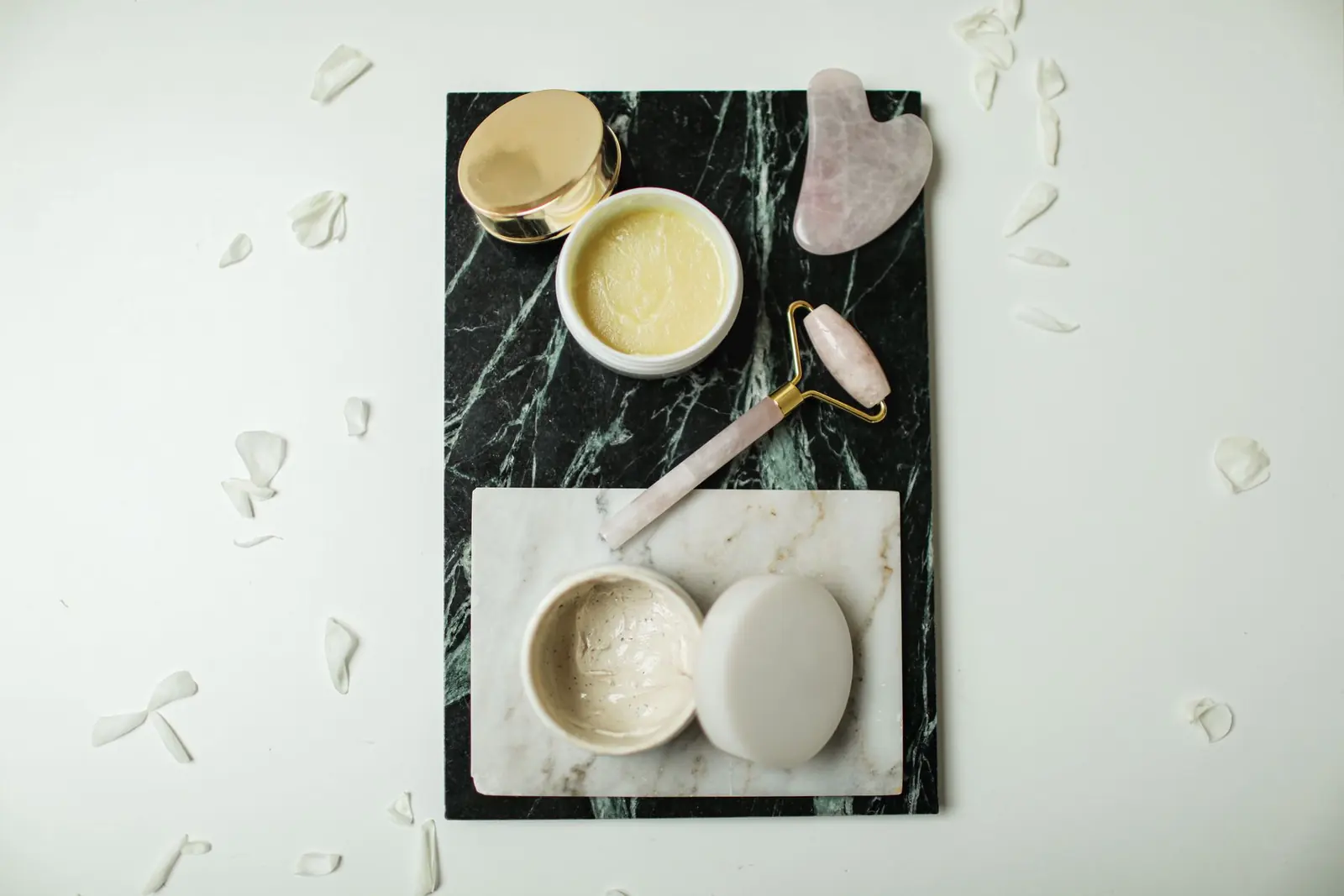 Open cream jars, a facial roller and gua sha stones on marble