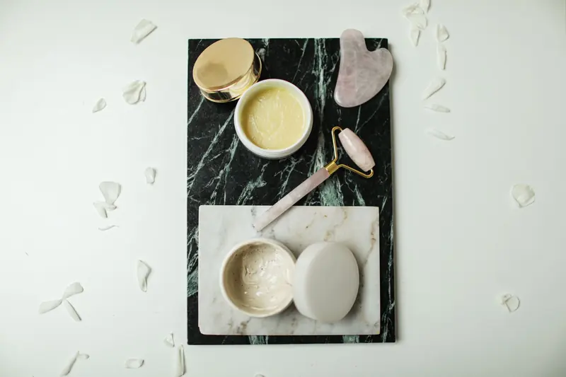 Open cream jars, a facial roller and gua sha stones on marble