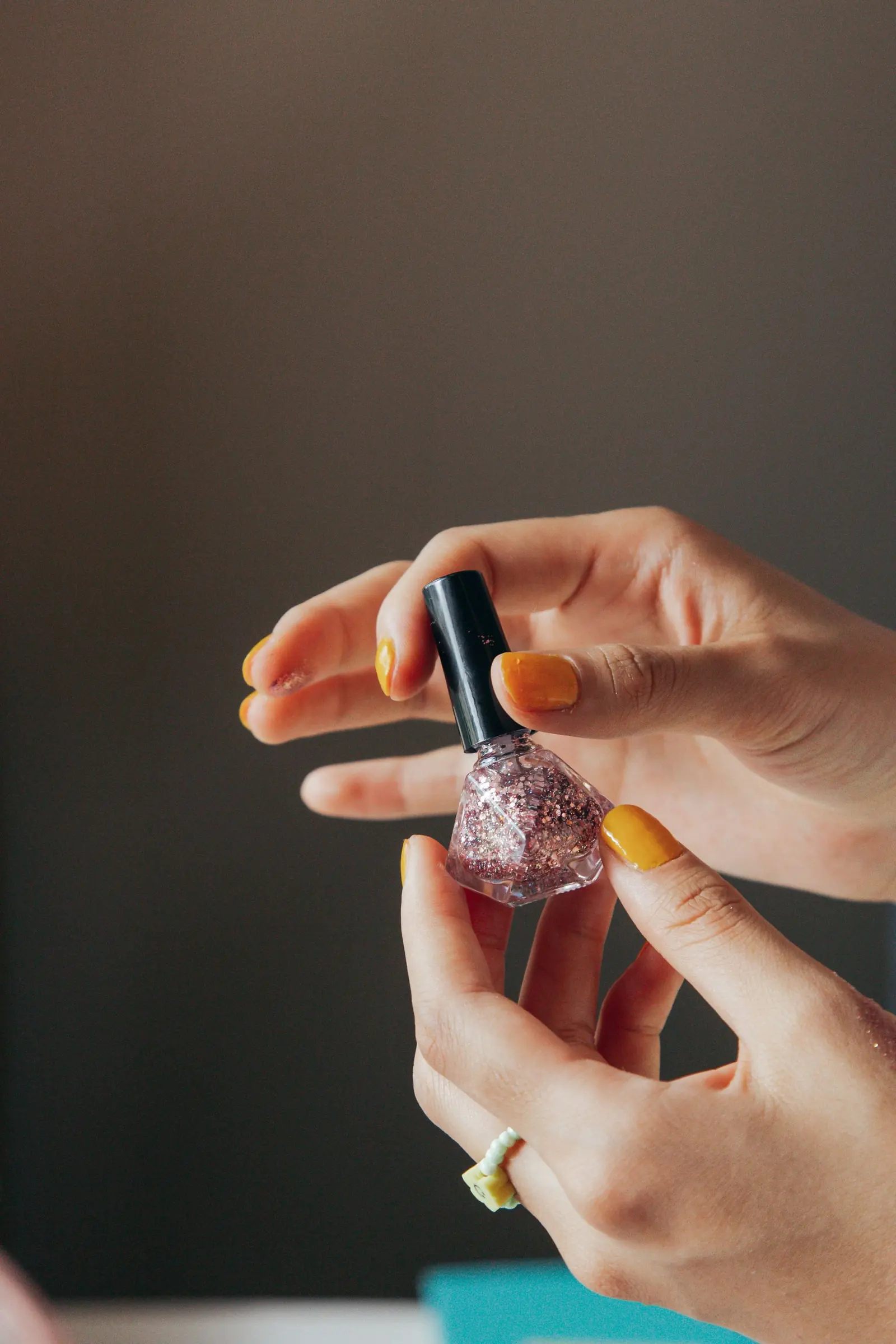 Hands opening a glittery nail polish bottle
