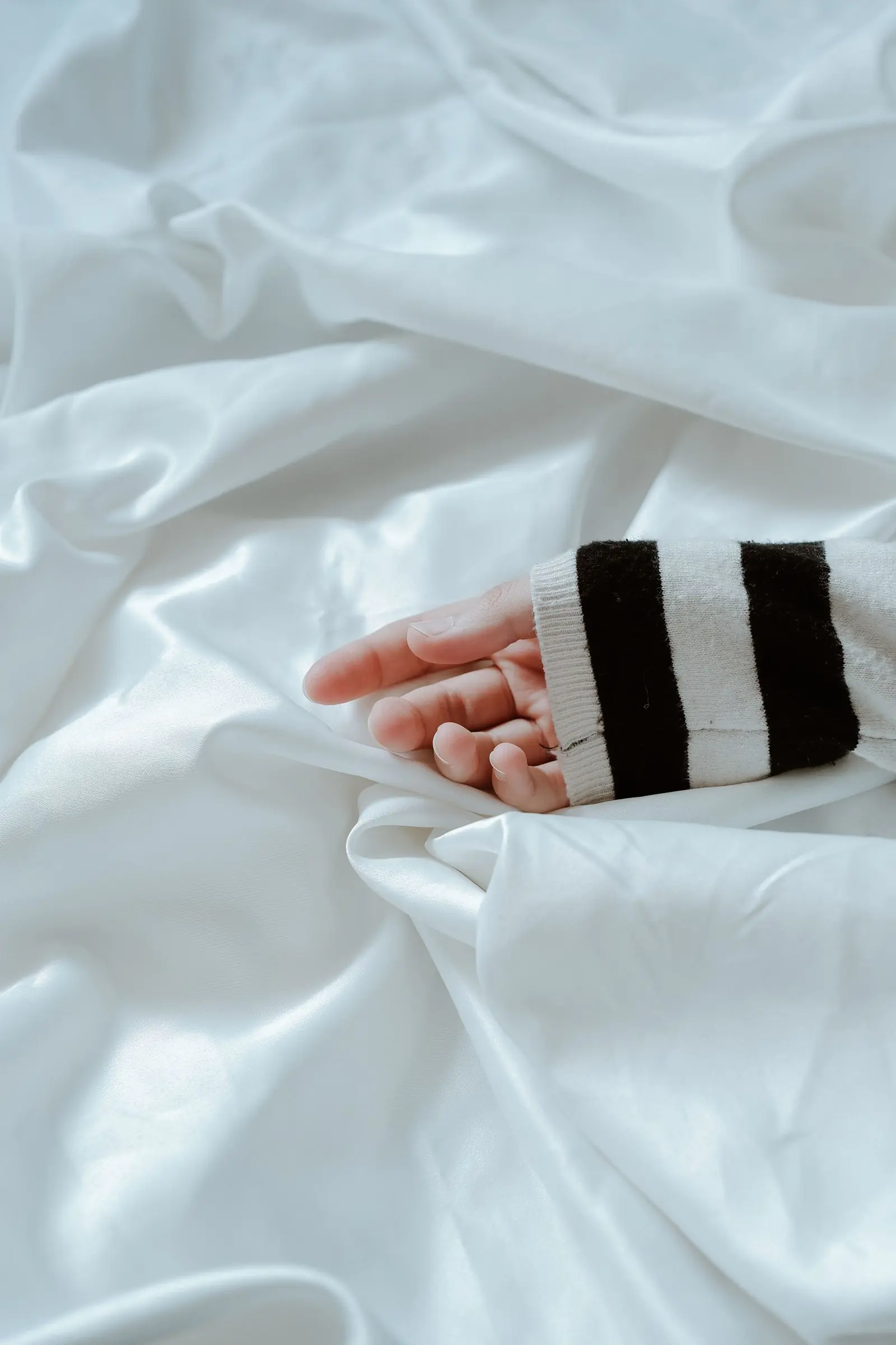 A hand resting on softly folded white satin sheets