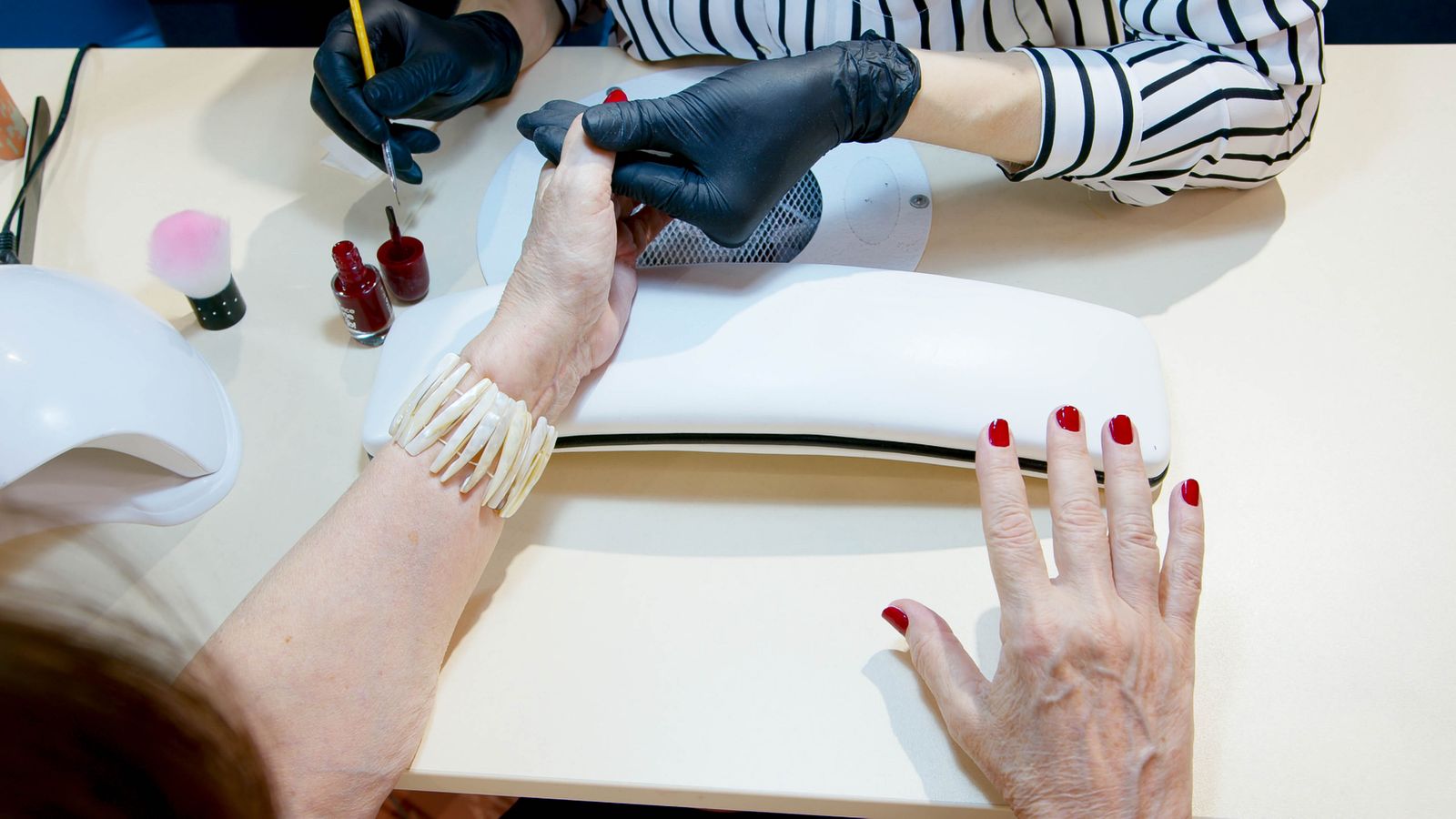 Overhead view of a nail technician applying red polish at a salon table