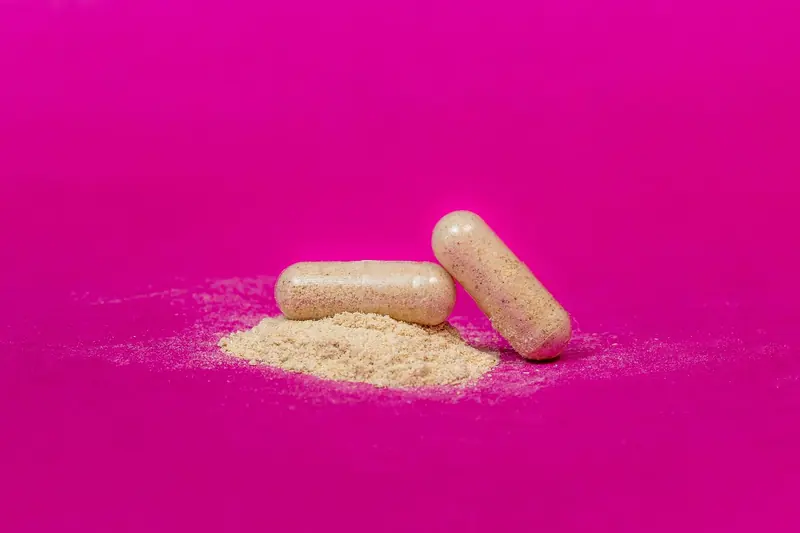 Close-up of two supplement capsules and powder on a vibrant pink background.