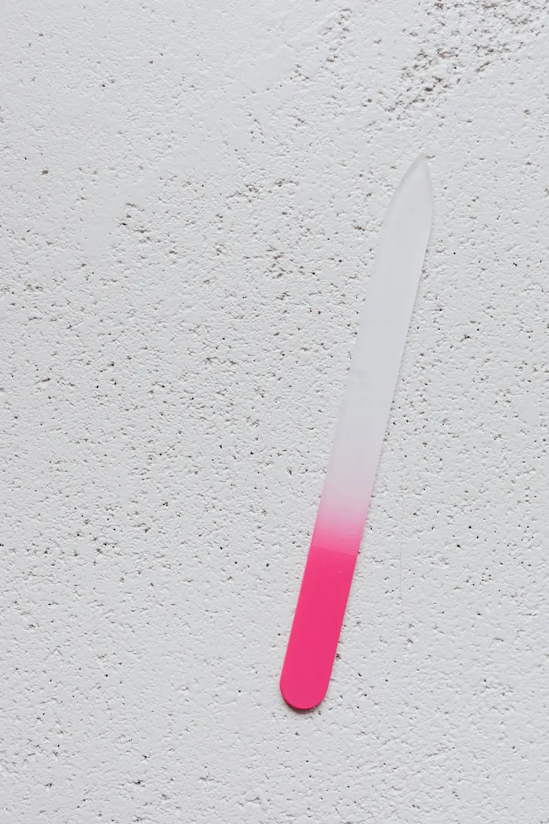 A pink and white nail file on a textured white surface