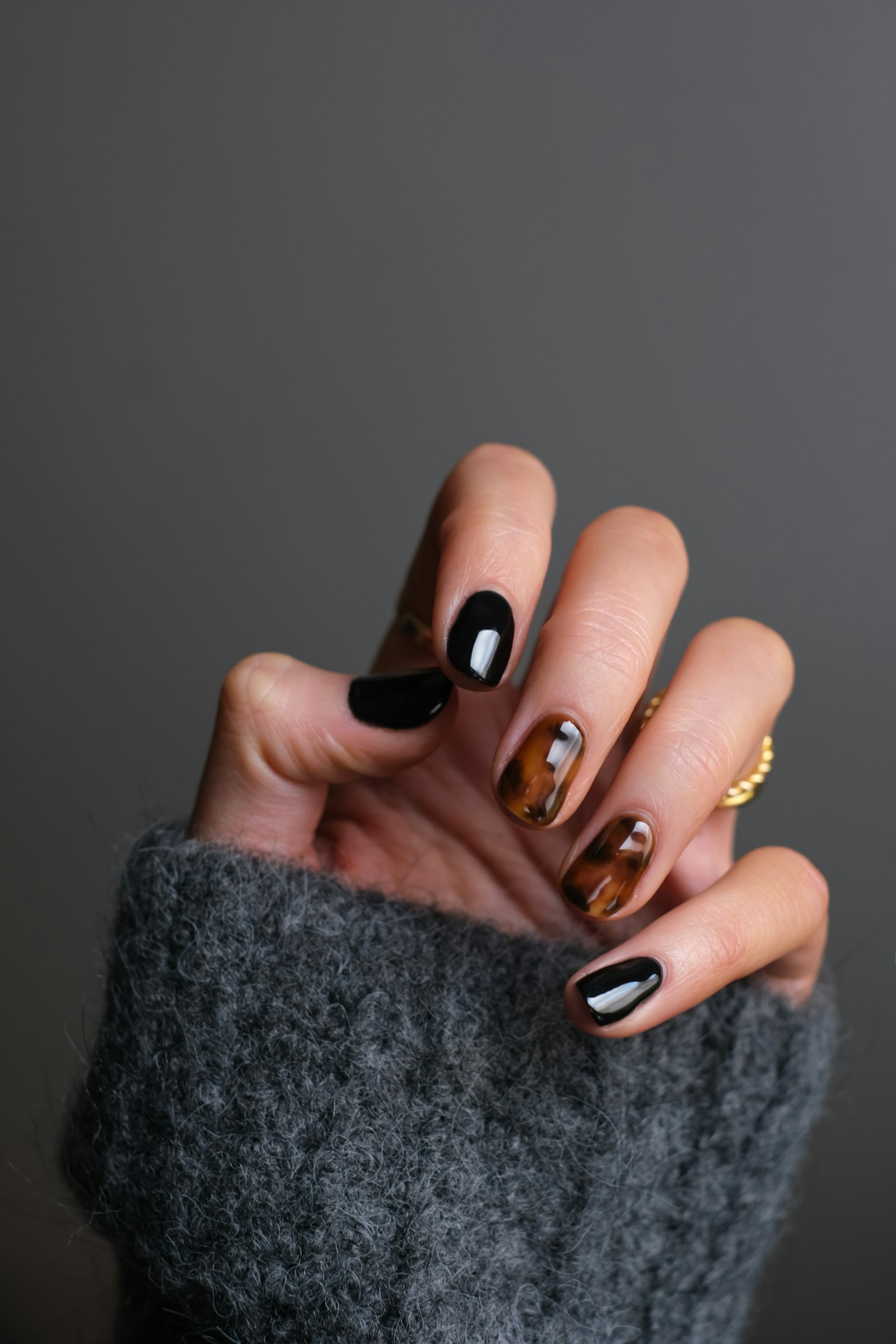 A hand with black and tortoiseshell nail art and a gold ring