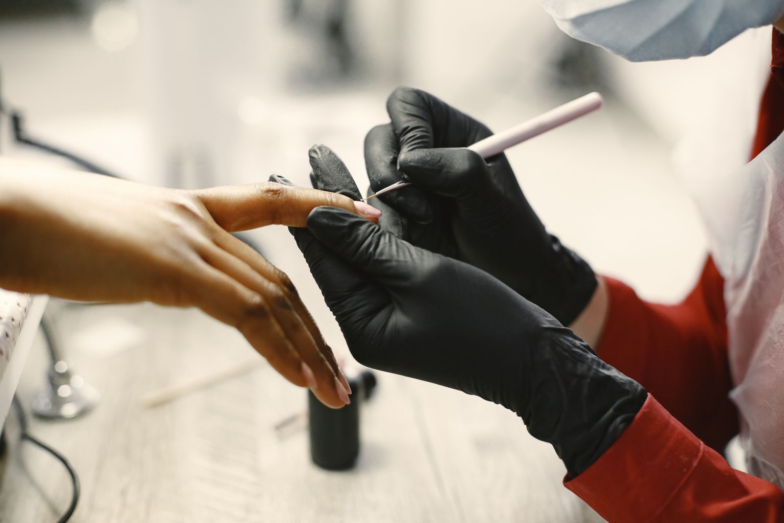 A nail technician in black gloves shaping a client's nails