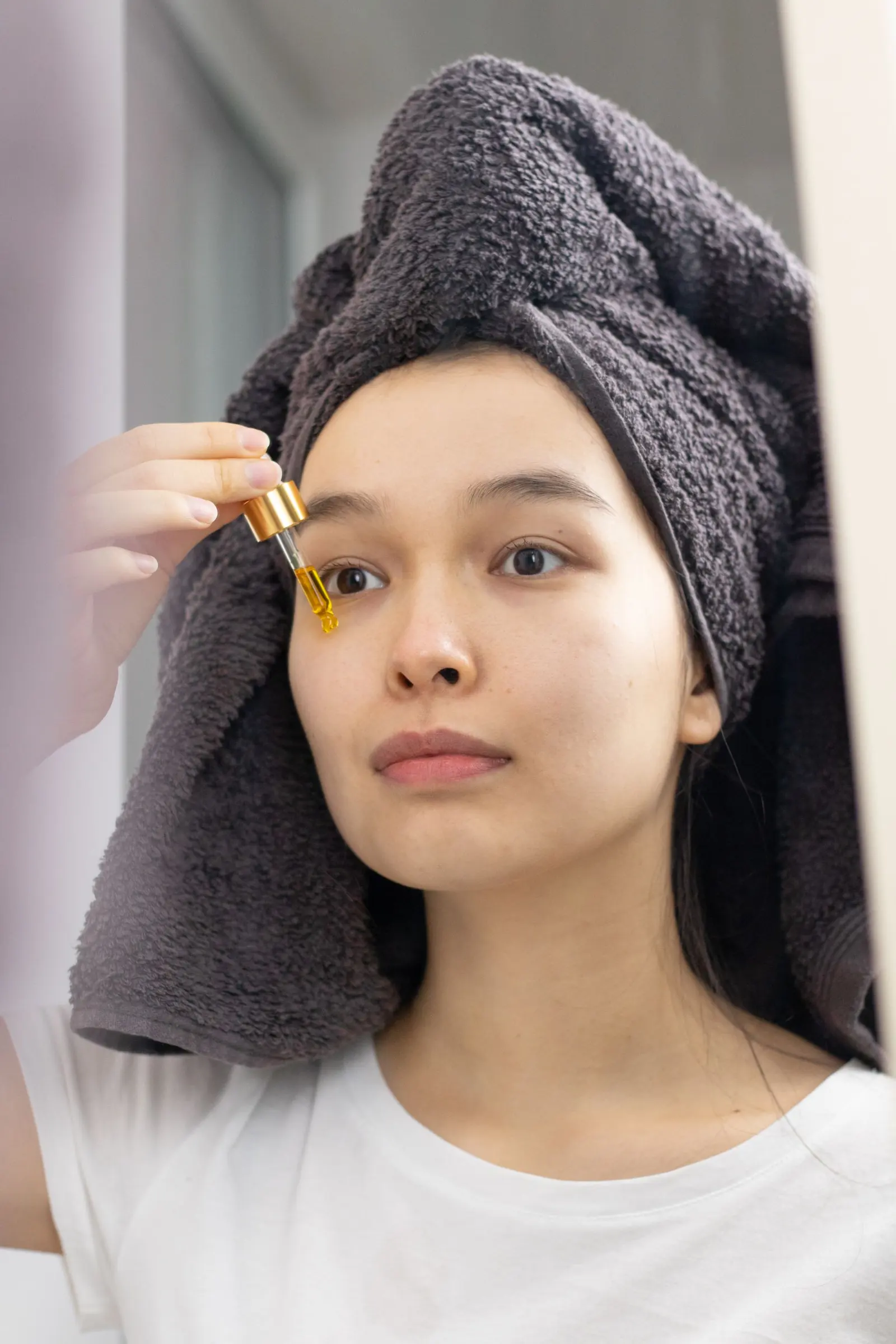 A woman with a towel on her head applying serum with a dropper