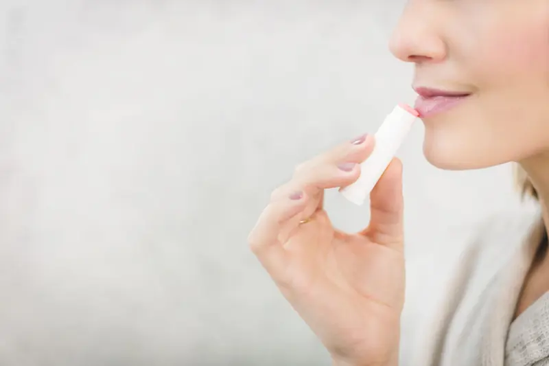 A woman applying lip balm to her lips
