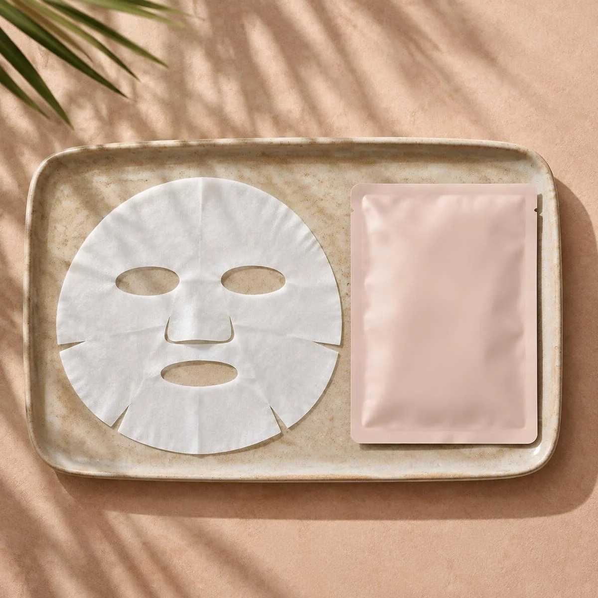Illustrative photo: Sheet mask beside a blank sachet on a ceramic tray